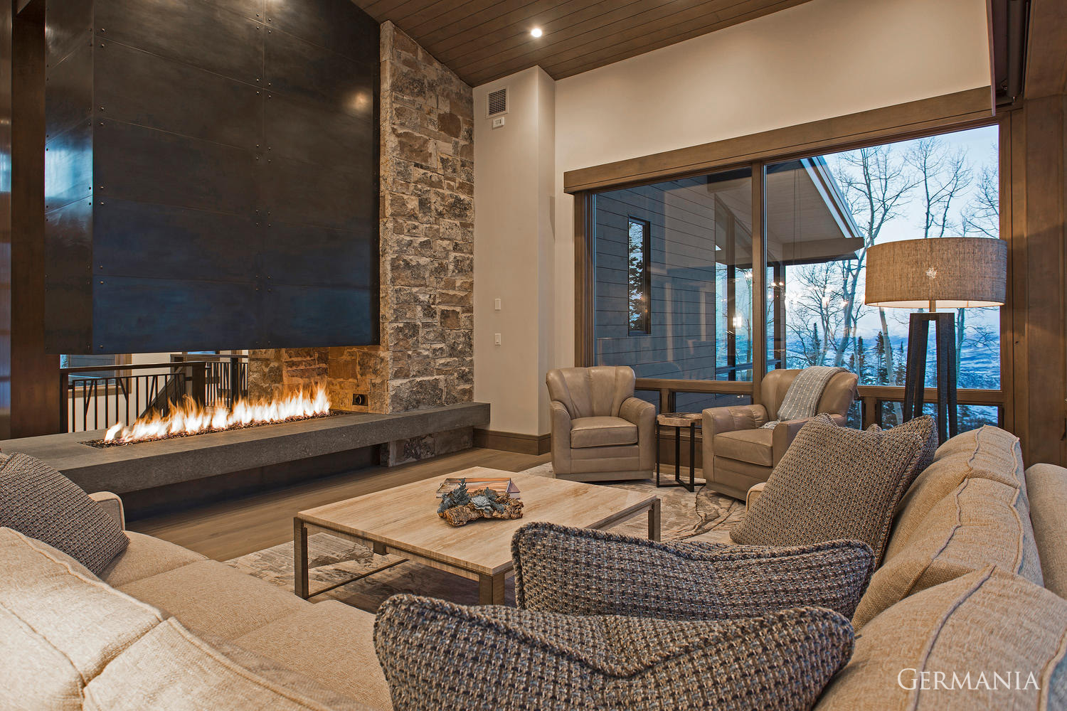 This custom house living room design features a carefully positioned fireplace and window shades to augment your entire mountain home living experience.