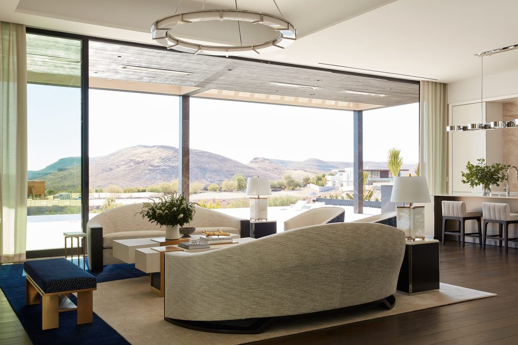 A wall of floor to ceiling windows floods this modern living room area with light.