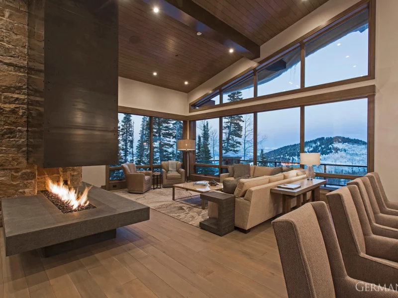A Park City, Utah luxury custom-built home's living room. High-end grey seating, fireplace, and dark wood accents fill the room.