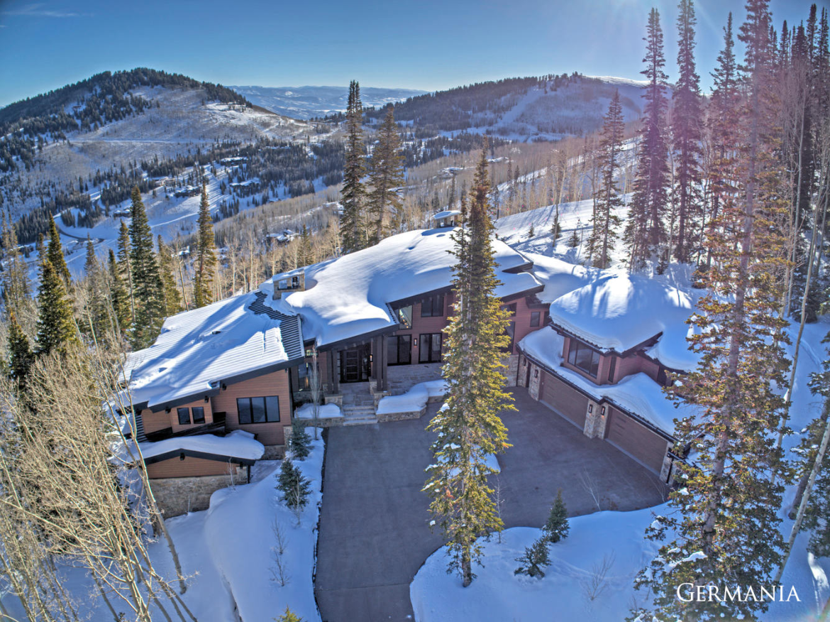 Luxury, custom-built home in The Colony Park City development in Park City, UT. The high-end home has large windows, a large driveway, and is covered in snow.