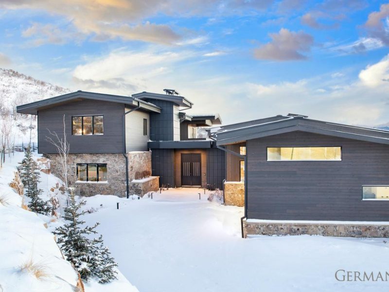 Luxury custom-built home in Park City, UT with dark grey paneling. Snow on the ground and hills surrounding it.