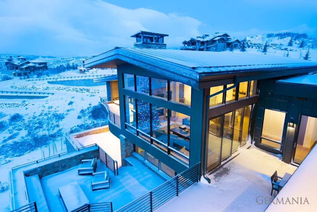 Custom-built, luxury, Park City, UT home nestled in the mountains and covered in snow. The home's large windows reveal a high-end interior and decorated christmas tree.